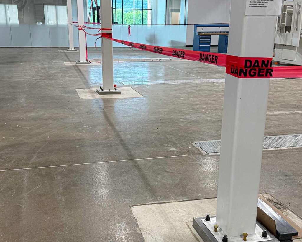 Interior warehouse slab area with steel columns secured and safety tape during structural upgrades
